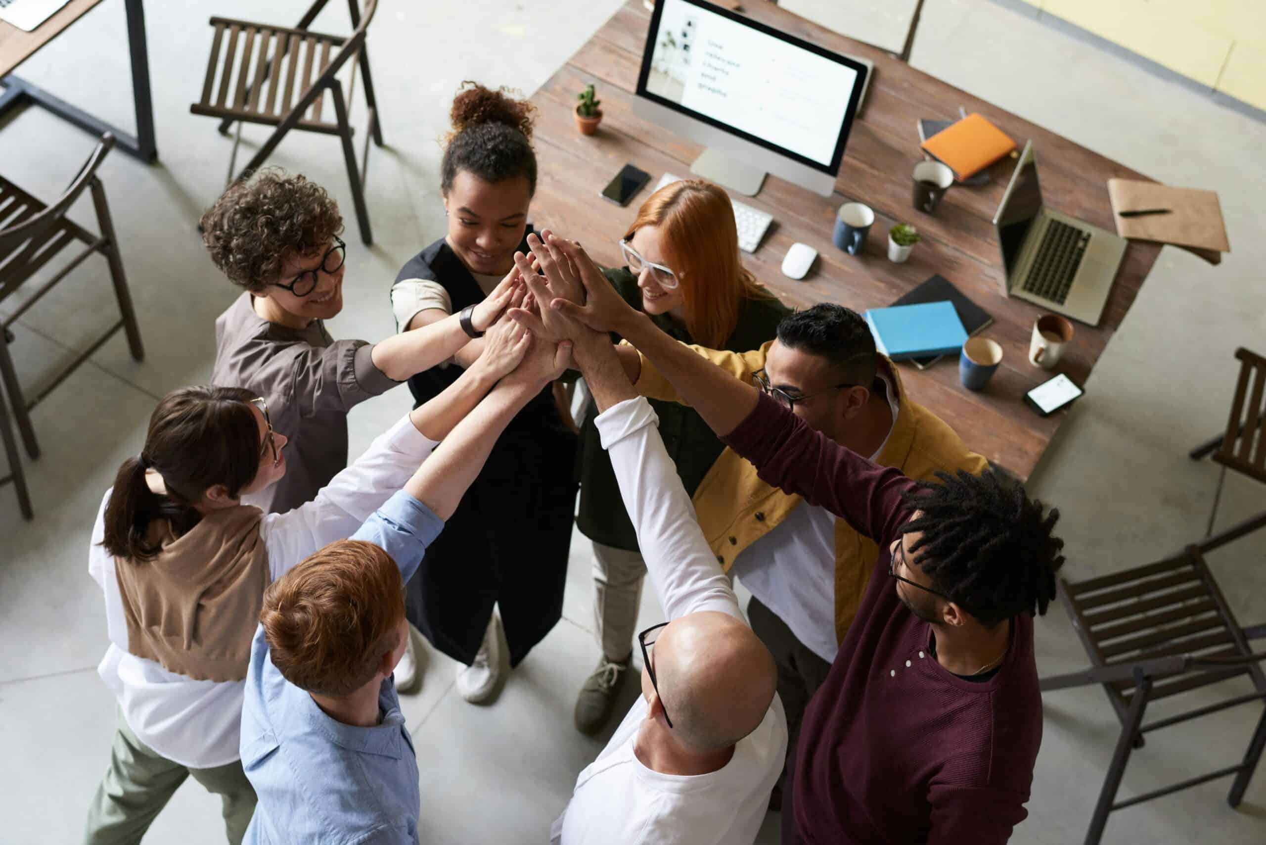 Team of diverse professionals giving high-five in a collaborative workspace.