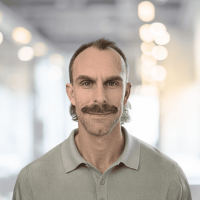 A professional man with a mustache and beard, smiling confidently in a modern, well-lit office envir.