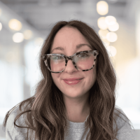 Woman with glasses smiling in a bright, modern office setting.