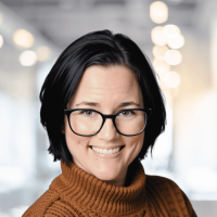 Smiling woman with glasses in a well-lit, modern office environment.