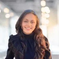 Smiling woman with long wavy hair, wearing a black top, in a bright, modern indoor environment.