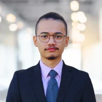 Professional business portrait of a young man in formal suit and glasses.